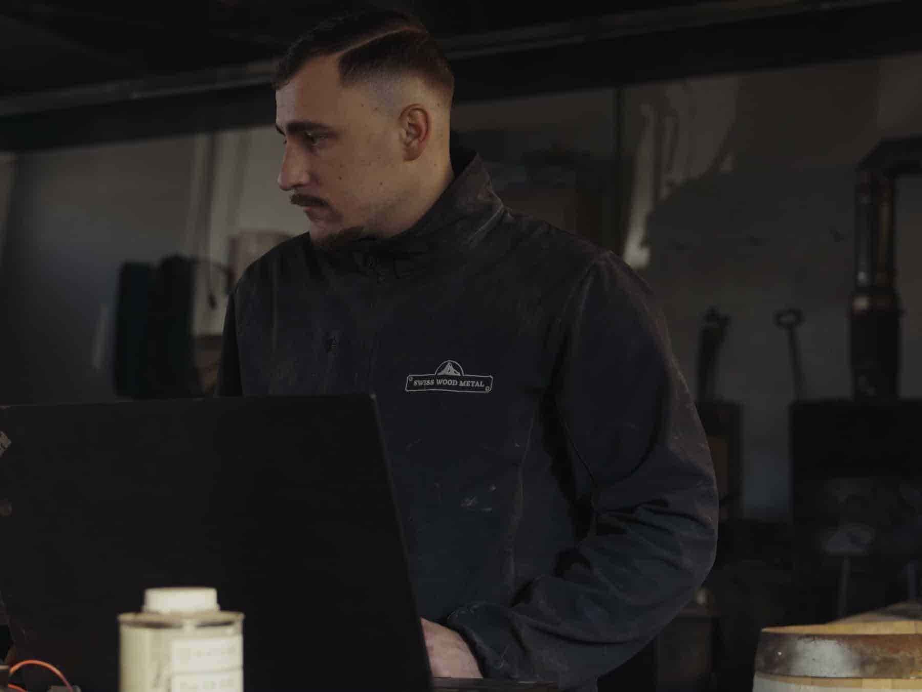 Jonas Caboussat devant son ordinateur, à côté de la fraiseuse CNC de l'atelier Swiss Wood Metal